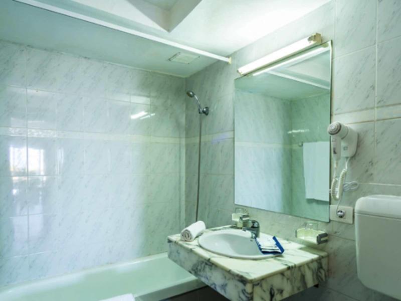 Helles Badezimmer mit Marmorwänden, Waschbecken, großem Spiegel und Wandföhn.