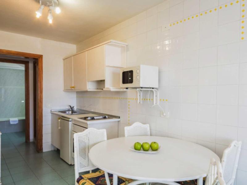 Helle Küche mit weißem Tisch, vier Stühlen, Mikrowelle und grüne Äpfel auf dem Tisch.