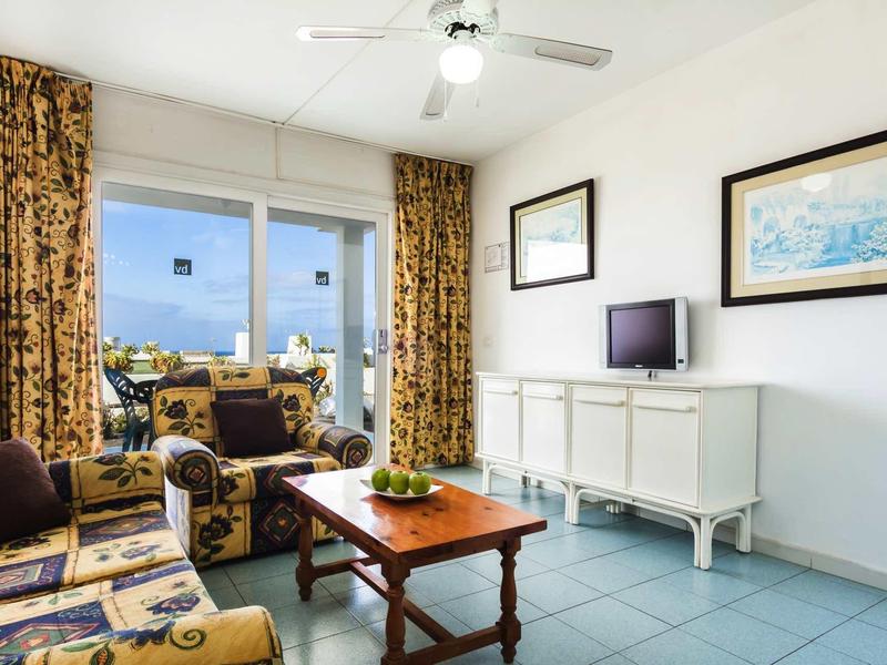 Helles Wohnzimmer mit floralen Vorhängen, gemusterten Sesseln, Holztisch und weißem Sideboard.