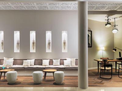 Moderner Wohnbereich mit langer grauer Couch, kleinen Hockern, Säule und Arbeitsbereich mit Schreibtisch.