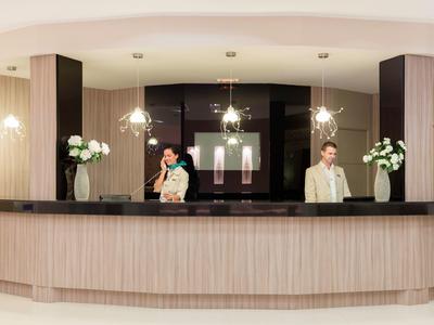 Hotelrezeption mit zwei Angestellten, moderner Tresen, helle Wände und Blumendekoration.