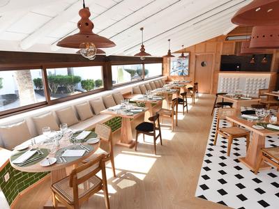 Ristorante luminoso con grandi finestre, mobili in legno e tavoli apparecchiati con stoviglie verdi.