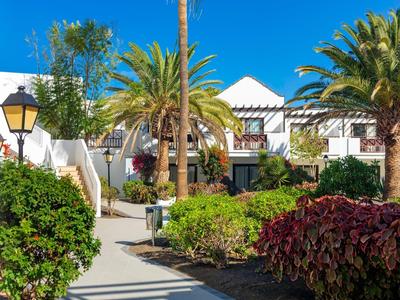 Hotelanlage mit weißen Gebäuden, Palmen und bunten Sträuchern bei klarem blauem Himmel.