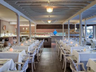 Großer heller Speisesaal mit weißen gedeckten Tischen, Holzstühlen und Deckenlampen.