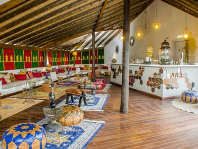 Großer, offener Raum mit Holzboden, farbenfrohen Sitzkissen, Teppichen und traditioneller Dekoration.