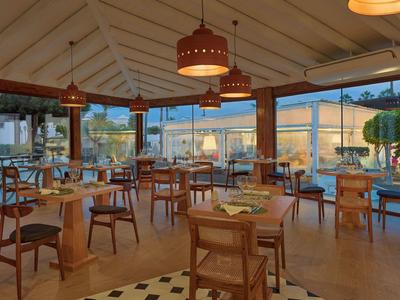 Hell eingerichteter Gastraum mit Holztischen, Stühlen und großen Fenstern zum Außenbereich.