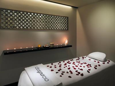 Una stanza massaggi tranquilla con un letto decorato con petali di rosa e luci di candele.