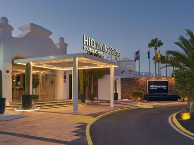 Ingresso di un hotel con area coperta, palme e insegna illuminata al crepuscolo.