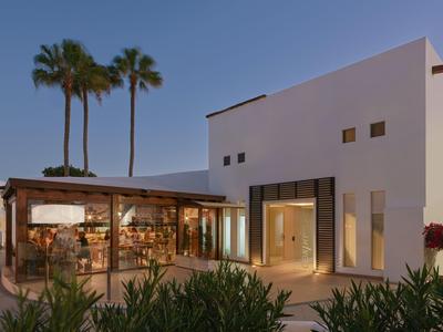 Edificio dell'hotel moderno con facciata bianca, area ristorante aperta e palme sullo sfondo.