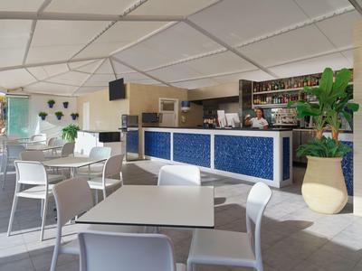 Area bar dell'hotel luminosa con arredi moderni e posti a sedere ai tavoli e al bancone.