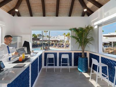 Area reception moderna con bancone blu e bianco e vista su piscina esterna e lettini.