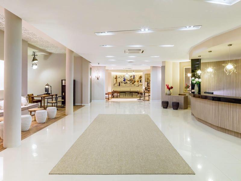 Großer heller Raum mit weißem Boden, langem Teppich, Holzmöbeln und Barbereich rechts.