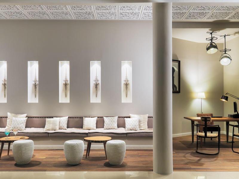 Moderner Wohnbereich mit langer grauer Couch, kleinen Hockern, Säule und Arbeitsbereich mit Schreibtisch.