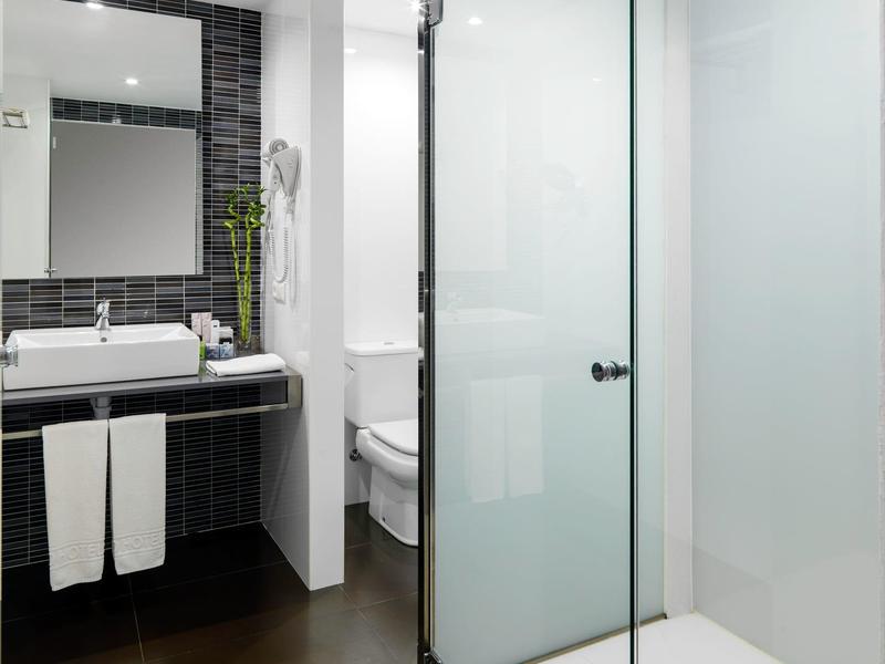 Modernes Badezimmer mit Dusche, Glaswand, Waschtisch, großem Spiegel und schwarzer Wandverkleidung.