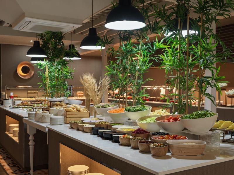 Großes Buffet mit verschiedenen Speisen, Pflanzen und modernen Lampen in einem stilvollen Raum.