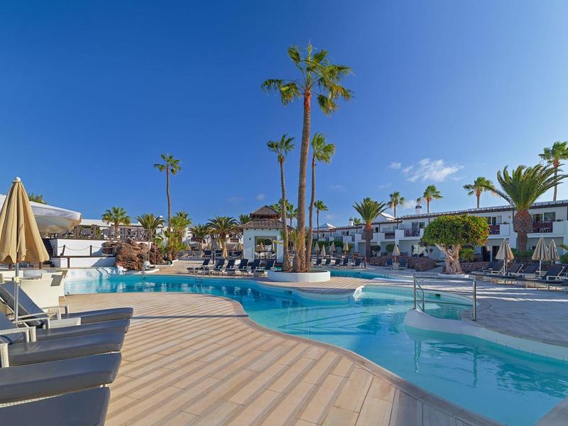 Moderner Hotelpool mit Liegen, Sonnenschirmen und Palmen unter klarem blauem Himmel.