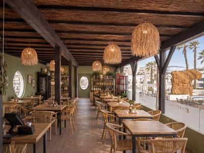 Innenraum eines hellen Restaurants mit Holztischen, Stühlen und natürlichen Lampenschirmen.
