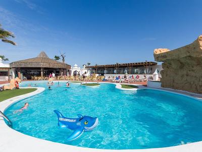 Klare blaue Schwimmbadwasser mit aufblasbarem Delfin und Hotelgebäuden im Hintergrund bei sonnigem Himmel.