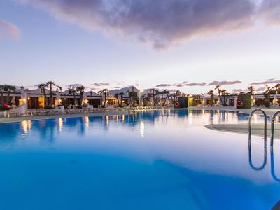 Großer, klarer Pool mit Treppe vor Reihen moderner Unterkünfte bei Sonnenuntergang.