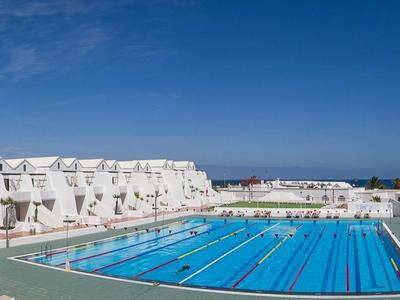 Großer Außenpool mit blauen Wasser und weißen Hotelgebäuden unter klarem Himmel.