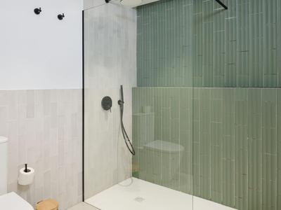 Moderne Dusche mit Glasabtrennung und grünen Wandfliesen in einem Badezimmer.