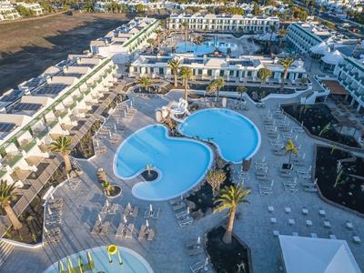 Vue aérienne d'un complexe moderne avec deux piscines reliées et des parasols.