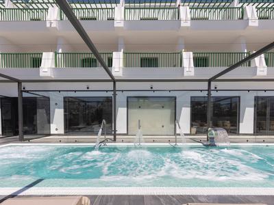 Whirlpool-Pool mit Sitzplätzen und Wasserturbulenzen vor einem Hotel mit Balkonen.