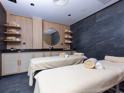 Moderner Massageraum mit zwei Liegen, hellen Holzmöbeln und dunklen Steinwänden.