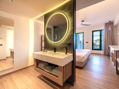 Modernes Hotelzimmer mit offenem Waschbeckenbereich, großem Spiegel und Blick zum Bett