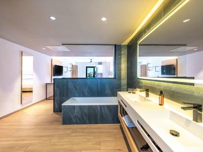 Modernes Hotelbadezimmer mit großer Badewanne, Doppelwaschbecken und großer beleuchteter Spiegelwand