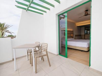 Balkon mit Tisch und Stühlen, Blick auf ein modernes Hotelzimmer mit offenem Türrahmen