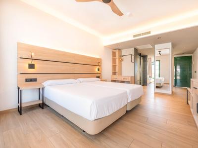 Helles Hotelzimmer mit zwei Einzelbetten, Holzboden und moderner Beleuchtung.