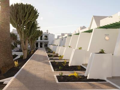 Weißes Terrassenhotel mit Pflanzen und einem breiten Gehweg an einem sonnigen Tag.