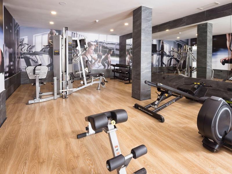 Heller Fitnessraum mit Holzfußboden, Kraftmaschinen, Spiegeln und Fotos an den Wänden.