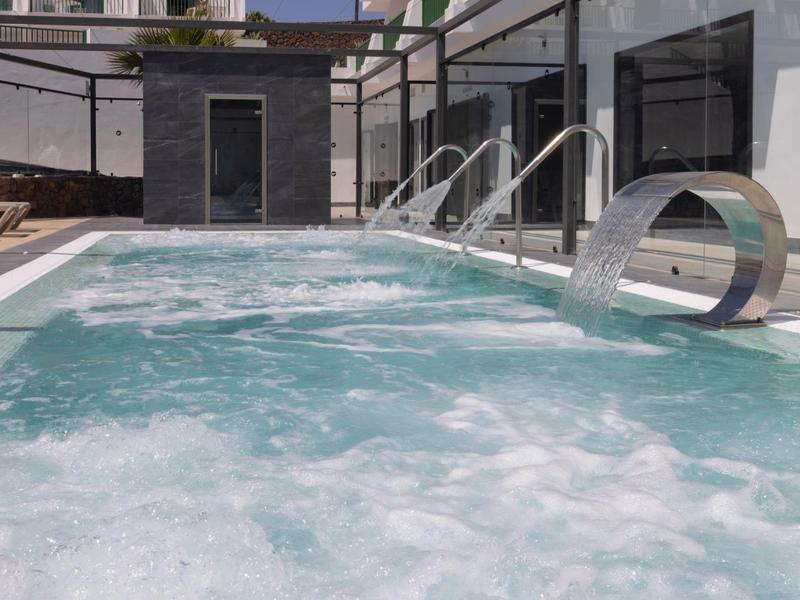 Moderner Whirlpool mit sprudelndem Wasser und Edelstahl-Düsen in hellem Außenbereich.