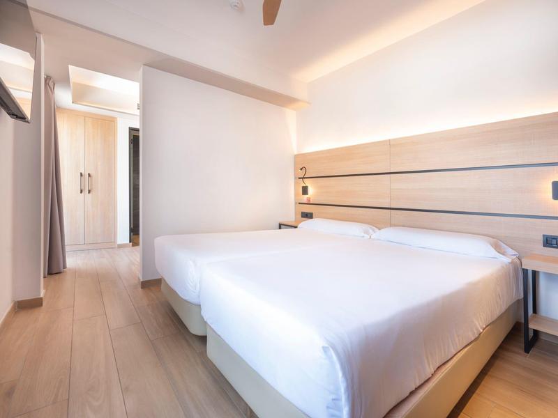 Helles, schlichtes Hotelzimmer mit Doppelbett, Holzfußboden und Schrank im Flur.