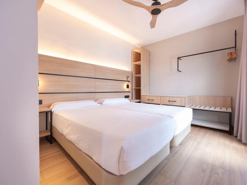 Modernes Hotelzimmer mit zwei Einzelbetten, Holzvertäfelung und Deckenventilator.