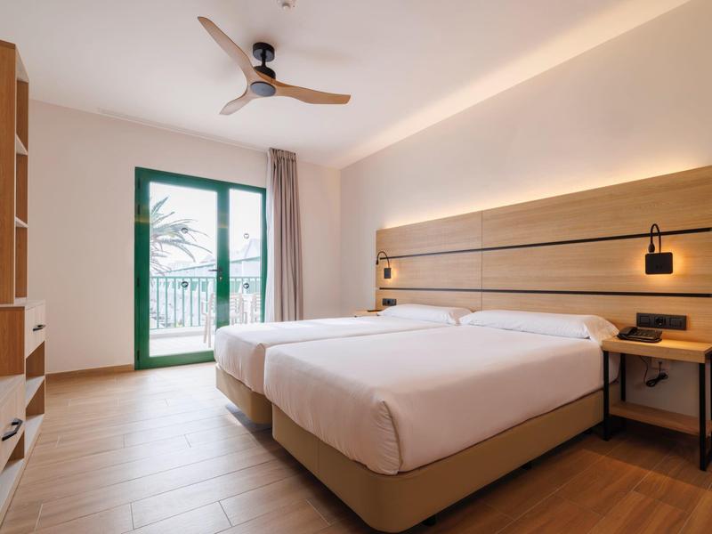 Modernes Hotelzimmer mit zwei Betten, Holzmöbeln und Balkon mit grünem Ausblick.