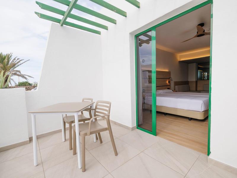 Balkon mit Tisch und Stühlen, Blick auf ein modernes Hotelzimmer mit offenem Türrahmen