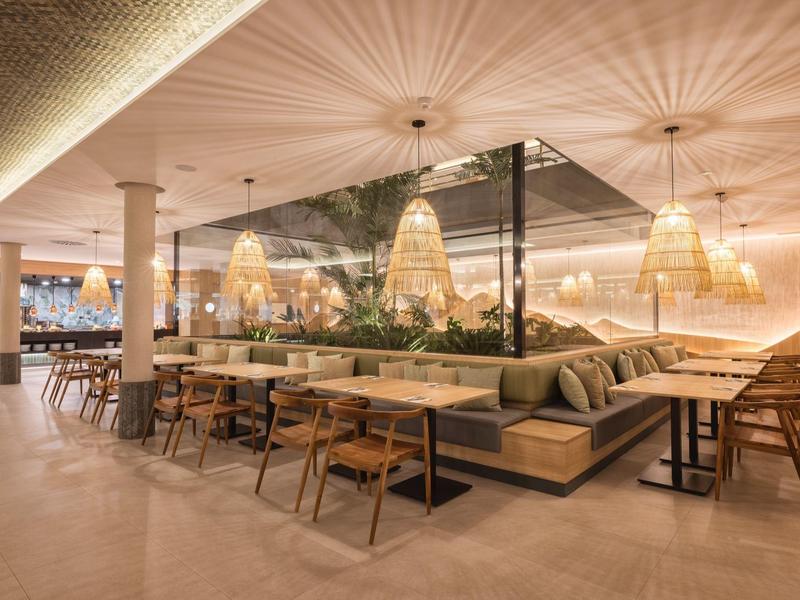 Modernes Restaurant mit hängenden Lampen, Holztischen und gemütlichen Sitzbereichen.