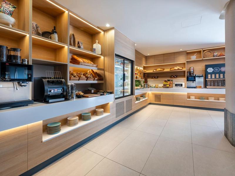 Heller Selbstbedienungsbereich mit Regalen voller Frühstücksartikel und modernen Geräten.