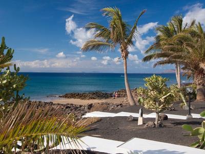 Tropische Küste mit Palmen, schwarzem Vulkansand und klarem blauem Meer unter blauem Himmel.