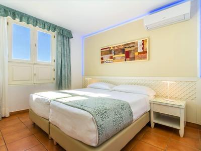 Helles Doppelzimmer mit zwei Einzelbetten, Nachttisch und Klimaanlage.