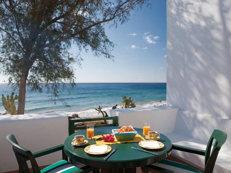 Balkon mit grünem Tisch und Stühlen, gedeckt mit Frühstück, Blick aufs blaue Meer und Himmel.