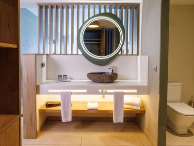 Modernes Badezimmer mit runder Spiegel, Waschbecken, Holzmöbeln und beleuchtetem Unterschrank.