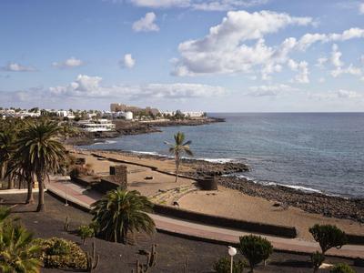 Küste mit Palmen, Sandstrand und felsiger Uferlinie unter blauem Himmel mit Wolken.