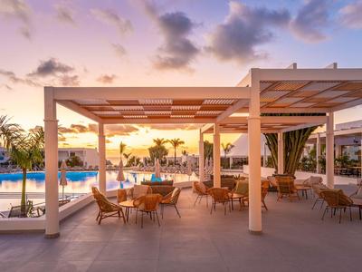 Zewnętrzny teren nowoczesnego hotelu z miejscami do siedzenia i basenem o zachodzie słońca.