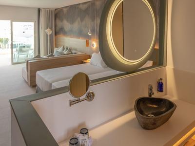 Modernes Hotelzimmer mit Doppelbett, Balkon, großem Spiegel und schwarzem Waschbecken in schlichtem Bad.