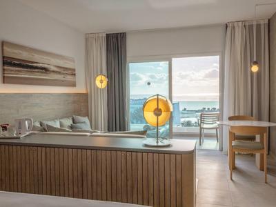 Modernes Hotelzimmer mit Bett, Sofa, Schreibtisch, großen Fenstern und Blick aufs Meer.