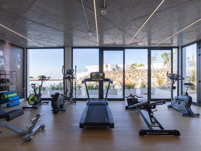 Nowoczesny sprzęt fitness w jasnym pomieszczeniu z dużymi oknami i widokiem na morze.